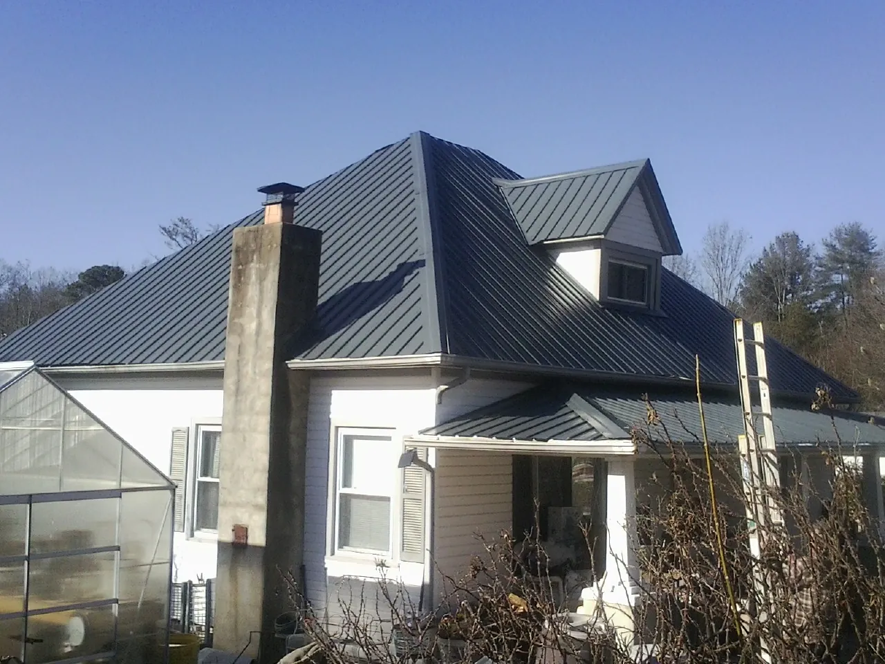 Dark blue standing seam metal roof on a white farmhouse with dormer — Slate & Tile Roof Repair by Roofing Brothers in Grassflat