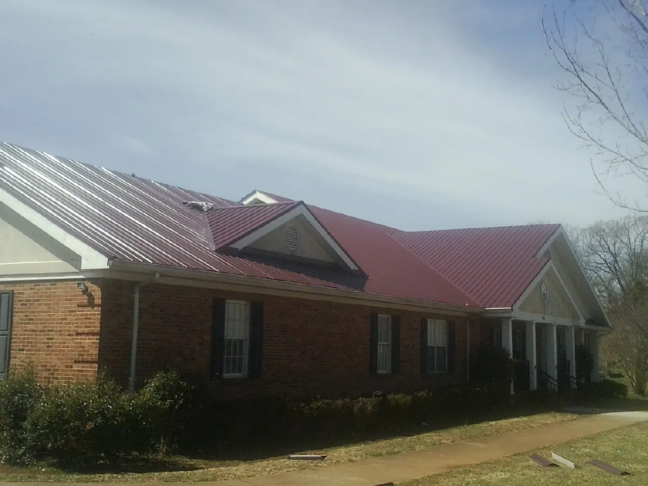 Red metal roof with gabled entries on a long brick building, from a Hail Damage Roof Repair job in Grassflat