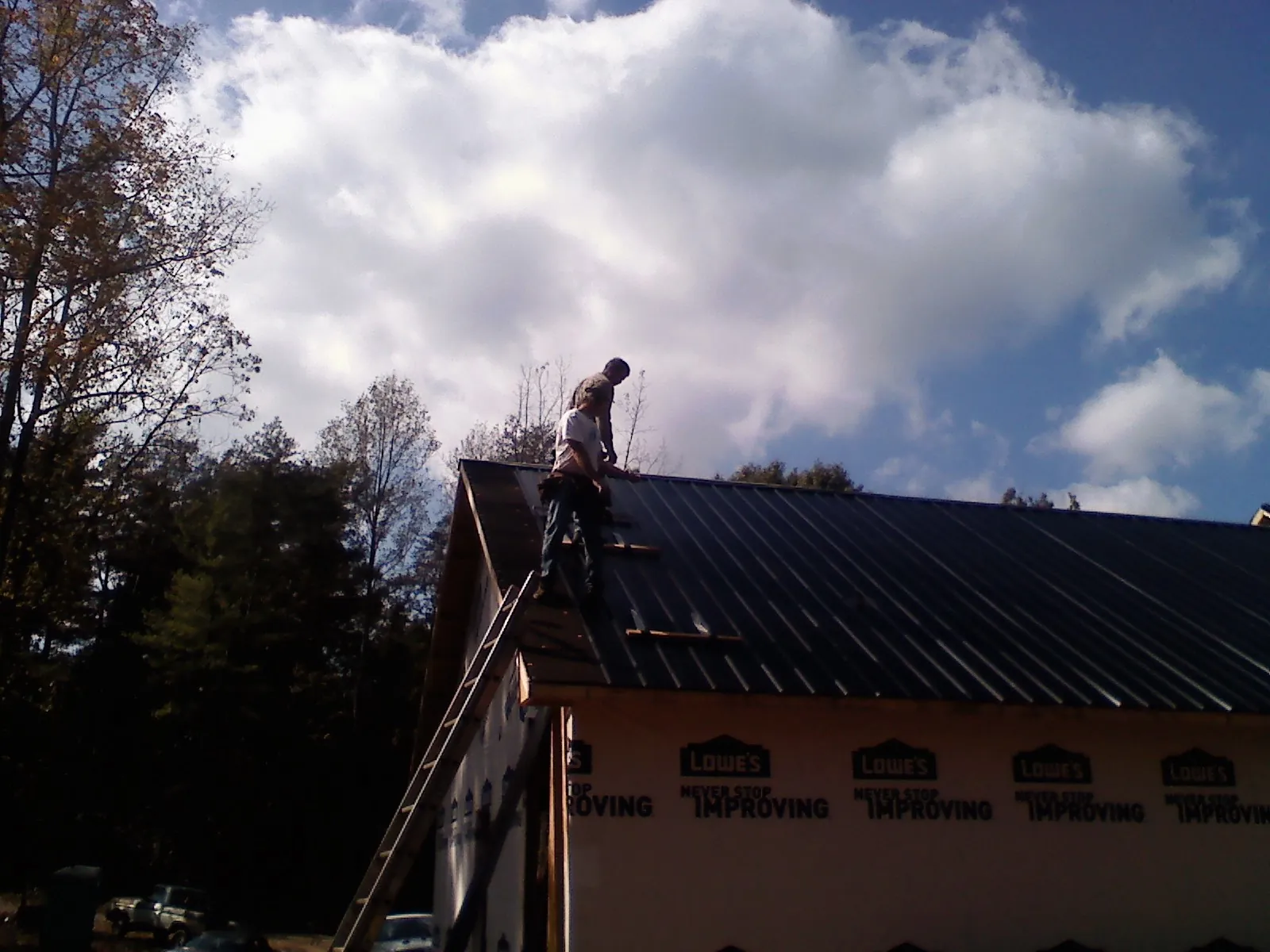 Roofer fastening dark metal panels high against a cloudy sky, from a Roof Inspection job in Grassflat